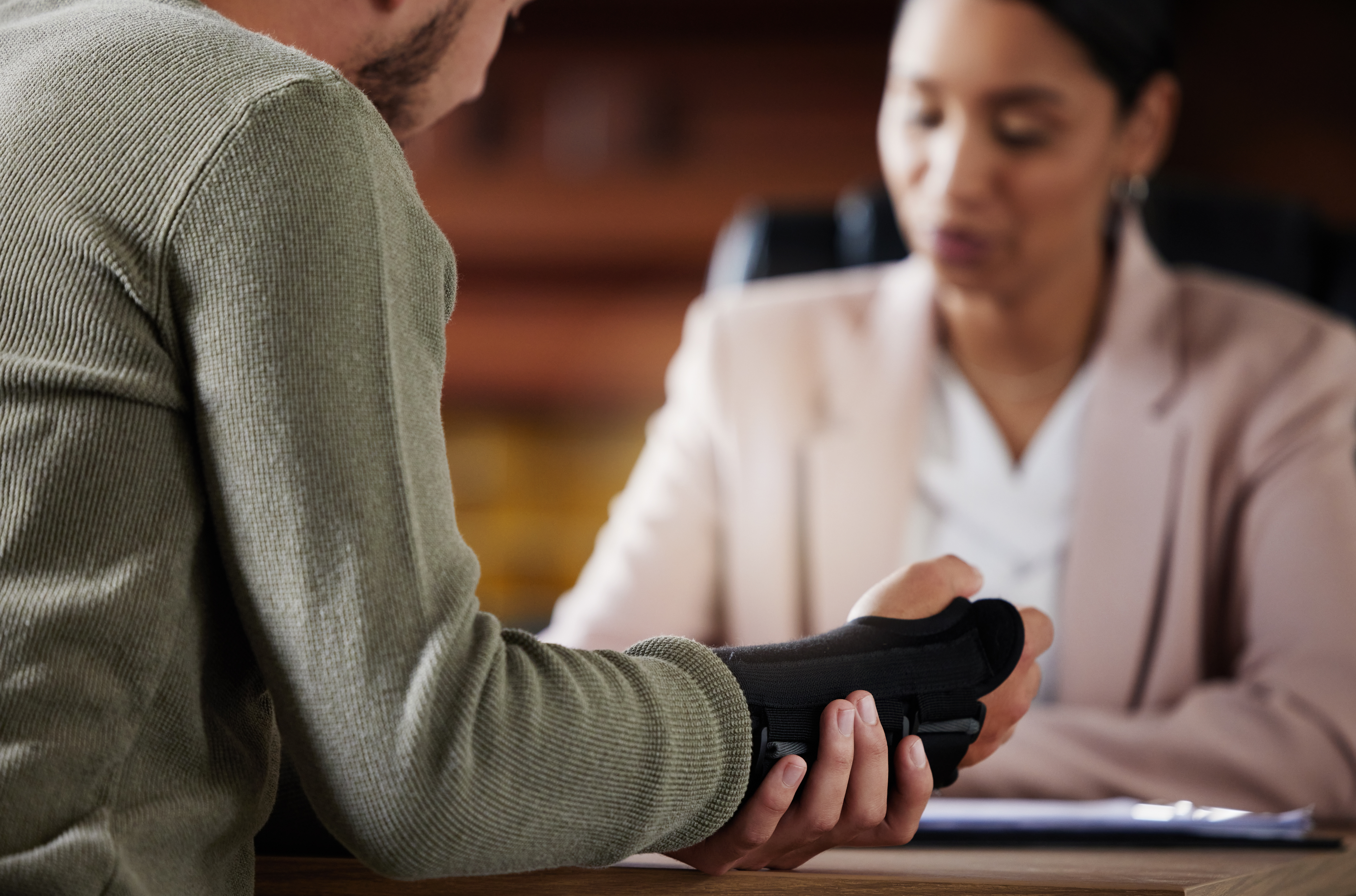 Man with a hand brace consulting a professional across a desk whether personal injury compensation is taxable following an injury claim.